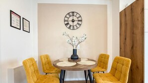 Un comedor con una mesa redonda, cuatro sillas, un reloj de pared y un jarrón con flores.
