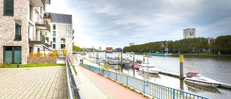 A riverside walkway with a paved path, a blue railing, and a row of boats docked along the water.