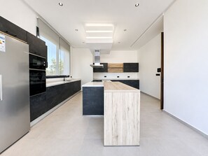 Et moderne køkken med en central ø, indbyggede apparater og et minimalistisk design.