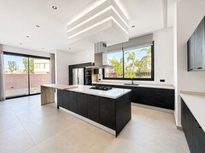 A modern kitchen with a central island, black cabinetry, and a large window offering a view of greenery. - Contemporary Elegance - Amelkis Golf Course - Elevator & Hammam (Marrakech)