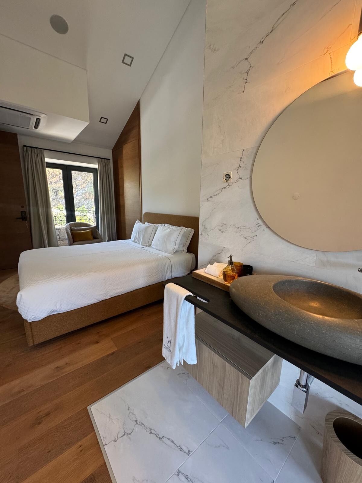 Une chambre d’hôtel moderne dotée d’un grand lit, d’une salle de bain avec un lavabo en pierre et offrant une vue sur l’extérieur.