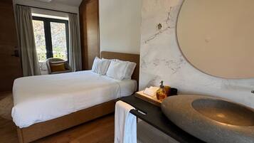 Une chambre d’hôtel moderne dotée d’un grand lit, d’une salle de bain avec un lavabo en pierre et offrant une vue sur l’extérieur.