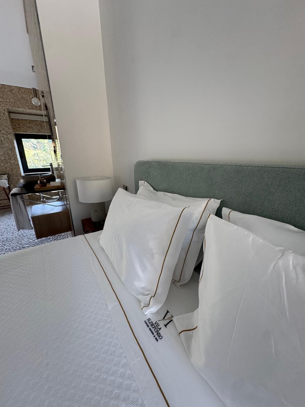 A hotel room with a bed, a nightstand, a lamp, and a window with a view.
