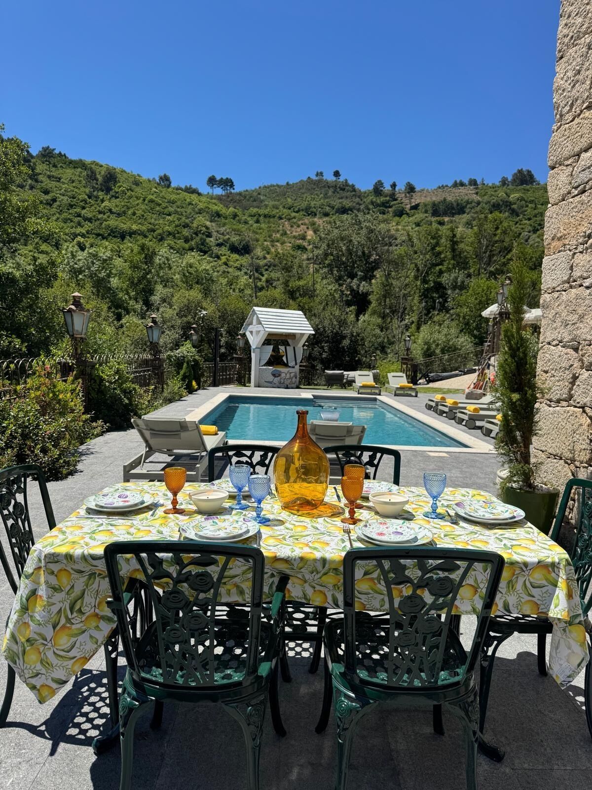 Un'area pranzo all'aperto con piscina, circondata da vegetazione e mura in pietra.