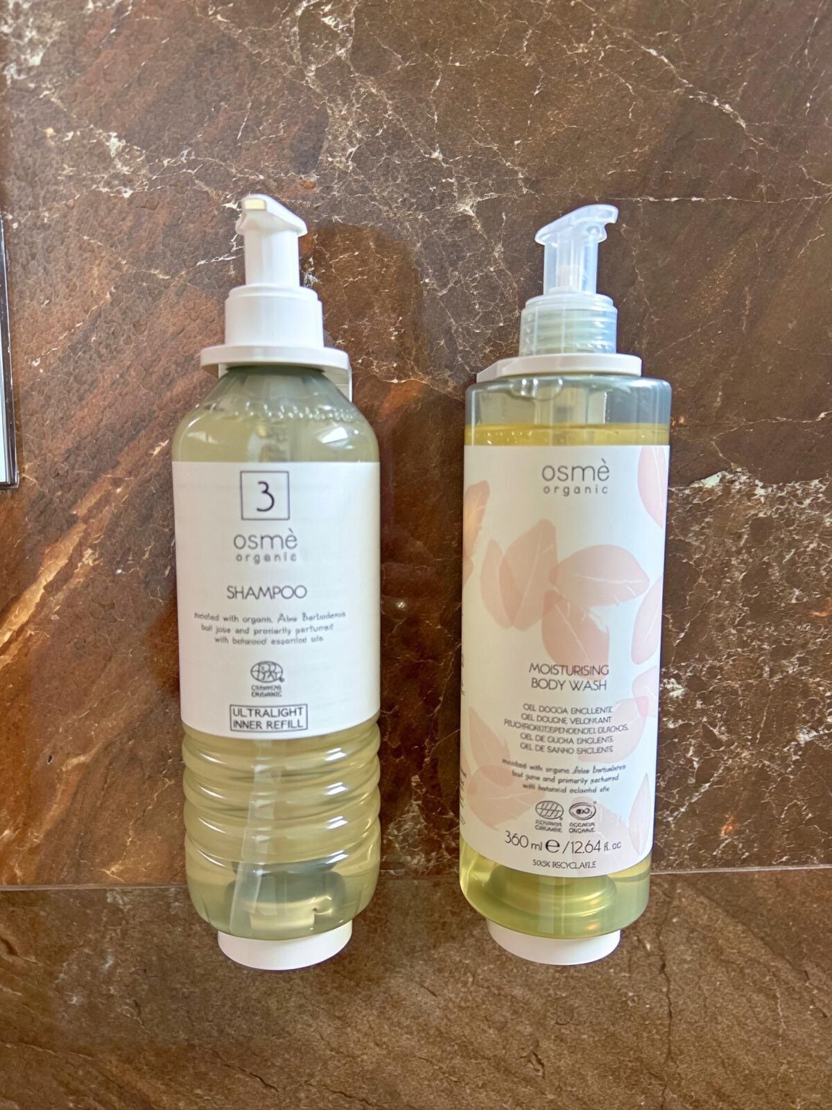 Dos botellas de champú y gel de baño orgánico Osmé sobre una superficie de mármol.