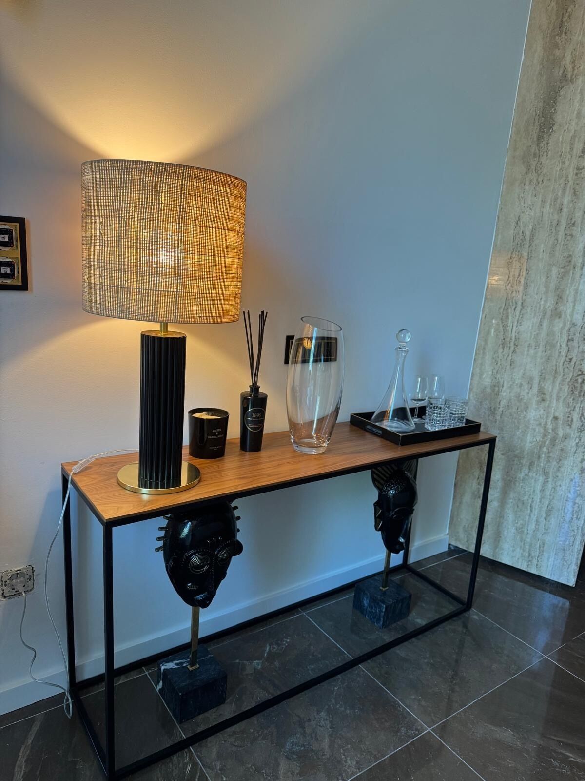 Un interior moderno con una consola de madera, una lámpara de fibras naturales y objetos decorativos.