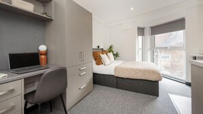 Ein modernes Schlafzimmer mit Schreibtisch, Bett und großem Fenster.
