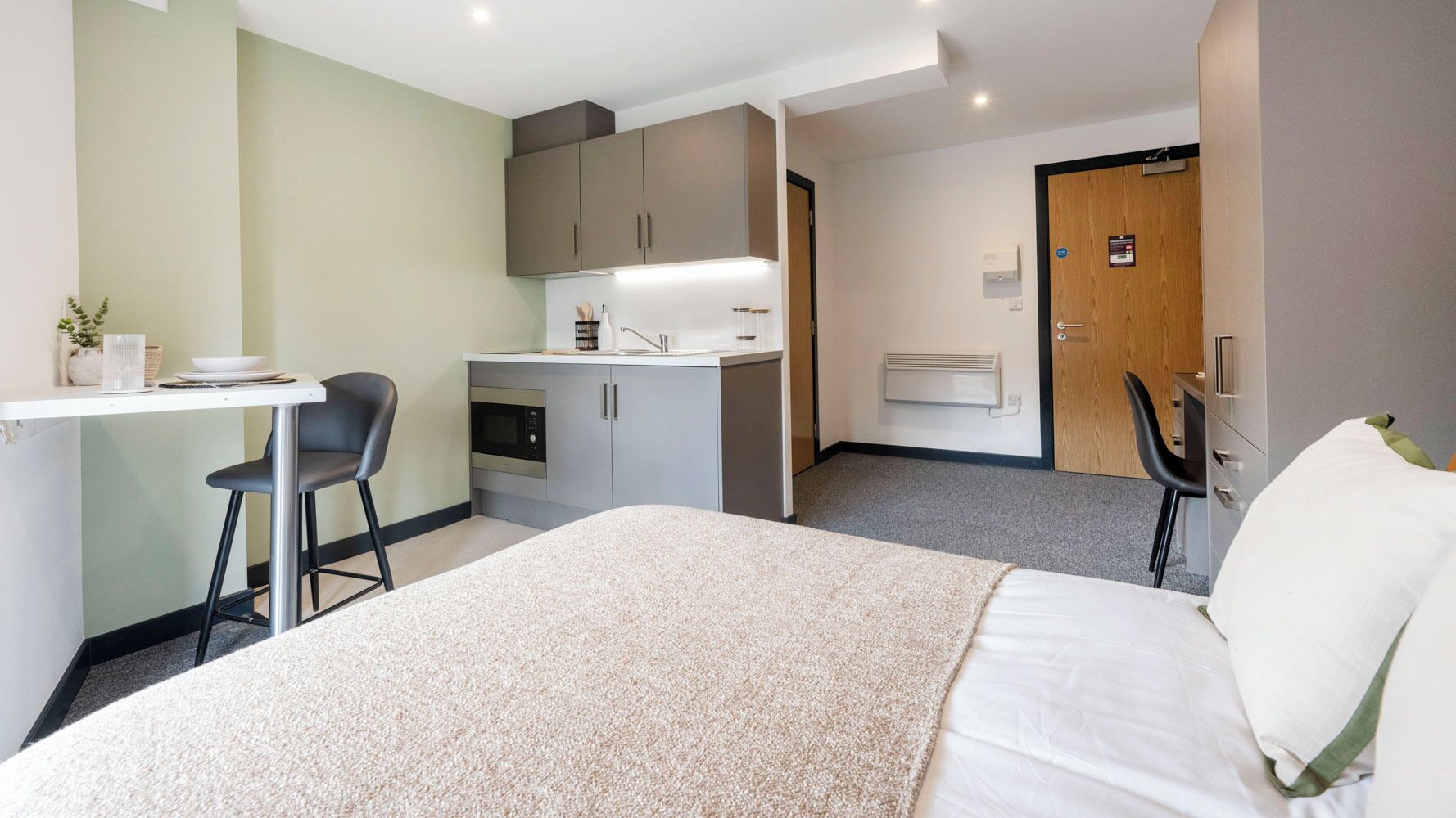 A hotel room with a bed, a desk, a chair, a kitchenette, and a bathroom.