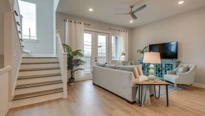 Ein modernes Wohnzimmer mit Treppe, einer Sofagarnitur, einem Fernseher und einem Deckenventilator.