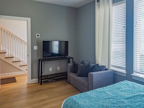 A room with a television on a stand, a grey sofa, a blue patterned bedspread, and a staircase. - Your Nashville home base-comfort close to downtown (Nashville)