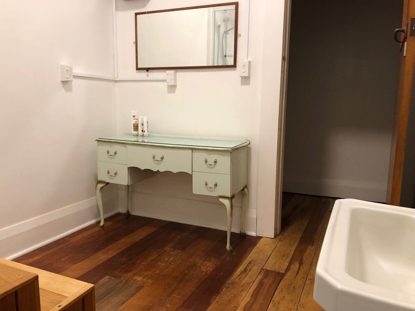 Een badkamer met een wit wastafel, een spiegel en een houten vloer.