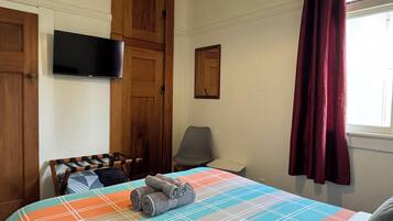 A bedroom with a bed, a television mounted on the wall, a wooden wardrobe, and a window with curtains.