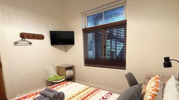 Una camera da letto con un letto, una sedia, una TV, una finestra con tende e un tavolino.