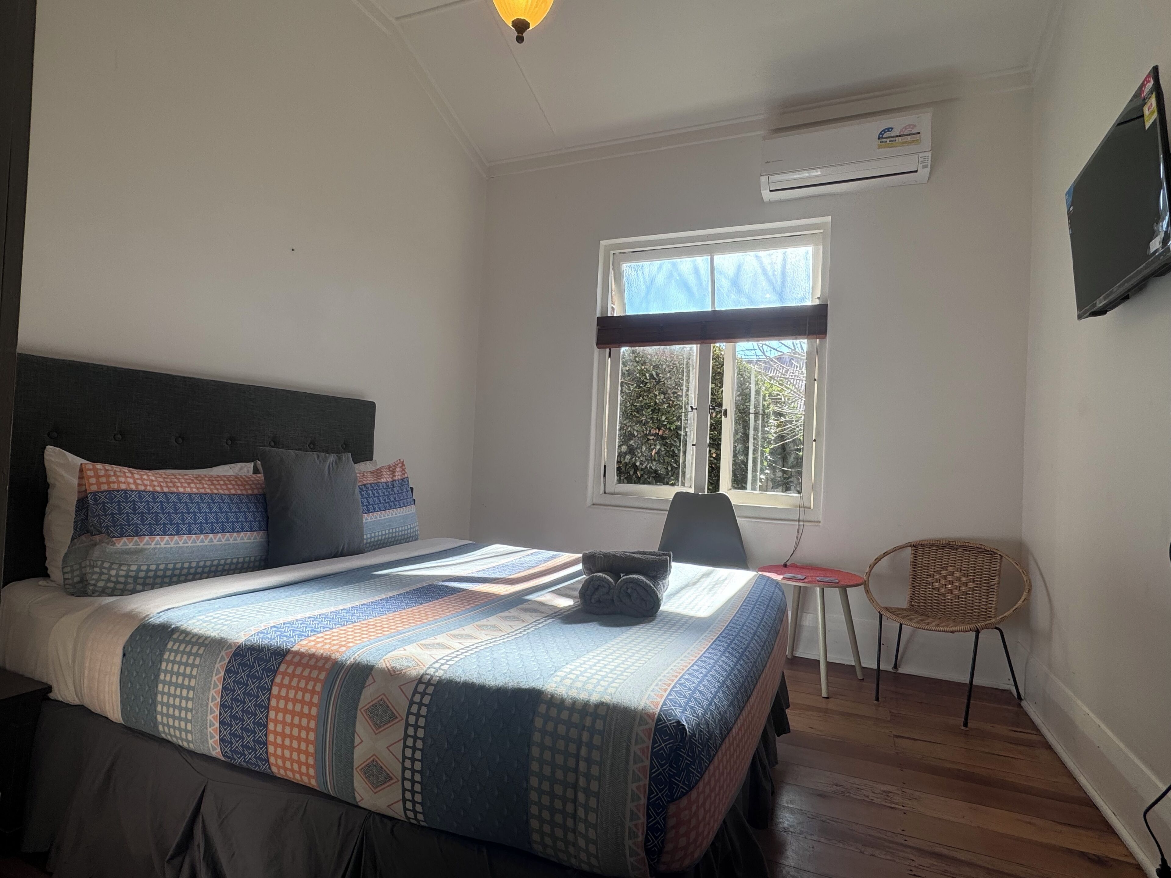 A bedroom with a bed, a chair, a window, and an air conditioning unit.