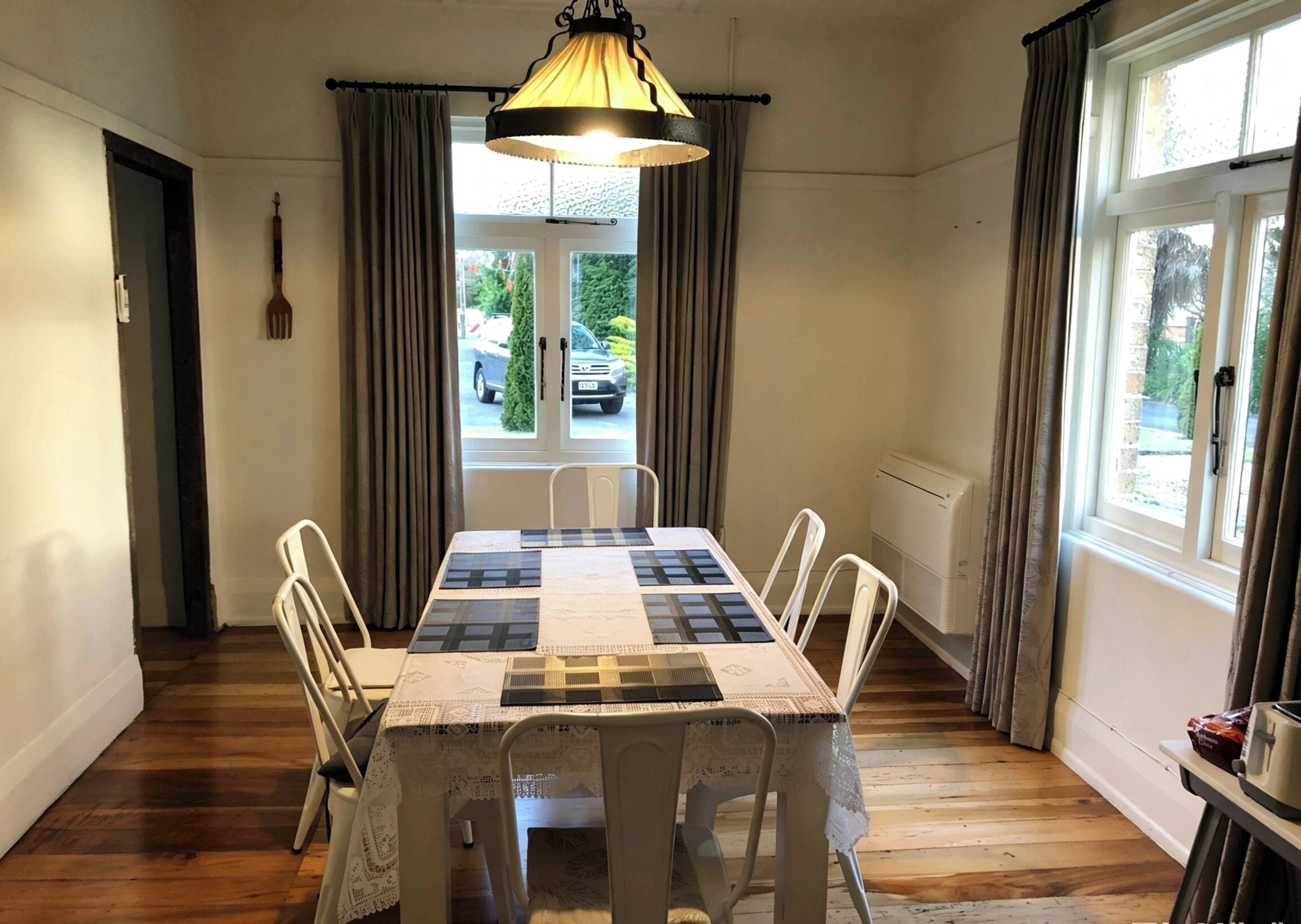 Un comedor con una mesa preparada para cuatro, sillas blancas, mantel estampado, lámpara colgante y vistas a través de una puerta de cristal.
