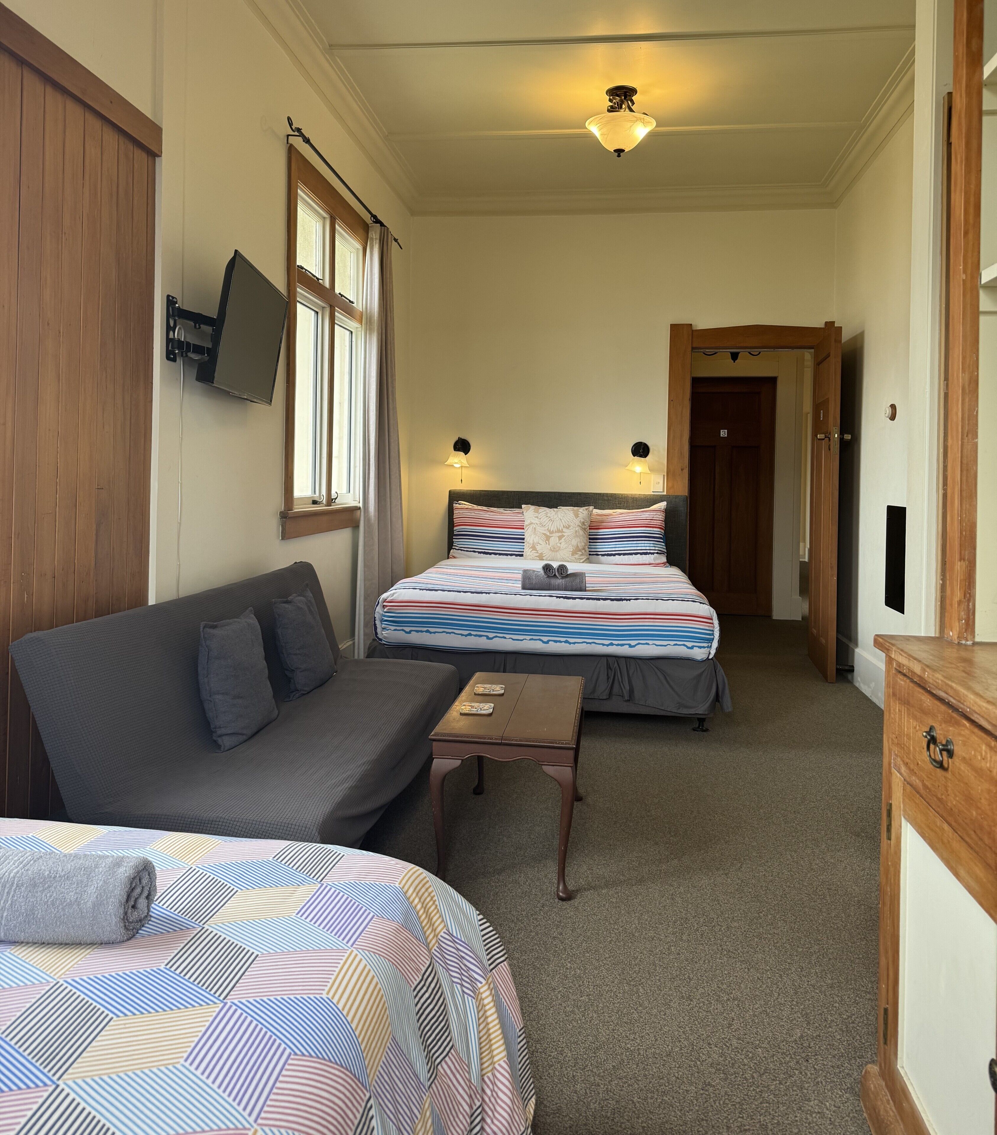 Una habitación de hotel con dos camas, un sofá, una mesita y un televisor montado en la pared.