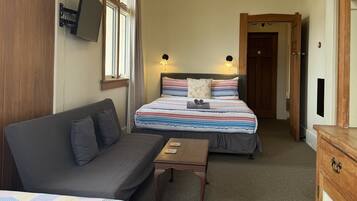Una habitación de hotel con dos camas, un sofá, una mesita y un televisor montado en la pared.