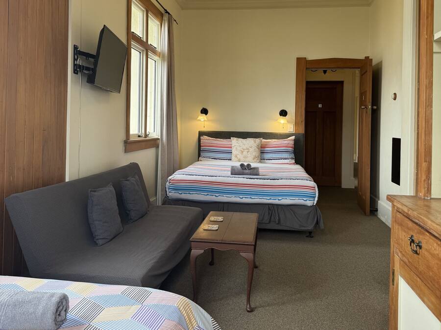 Una habitación de hotel con dos camas, un sofá, una mesita y un televisor montado en la pared.