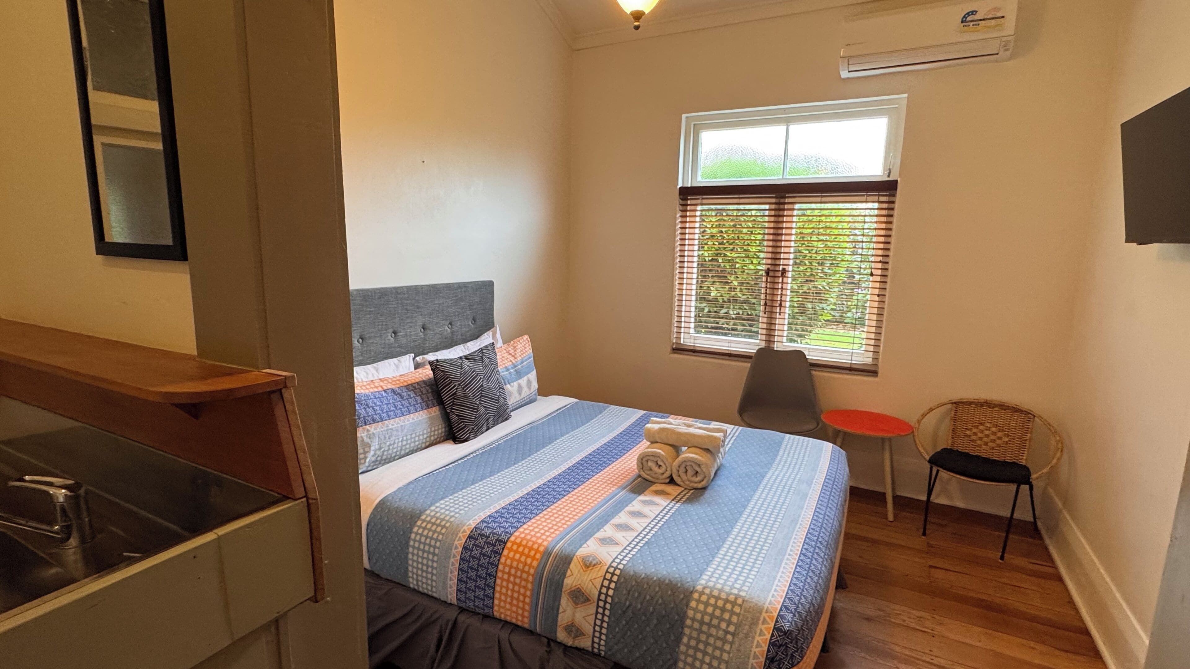 A bedroom with a bed, a chair, a small table, and a window with blinds.