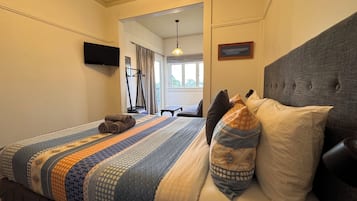 Habitación de hotel con cama, televisor de pantalla plana montado en la pared, ventana con cortinas y una mesita.