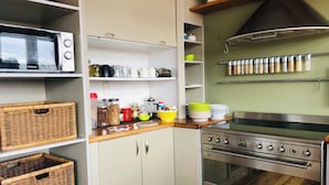 A kitchen with a microwave, stove, and various storage shelves. - Penmarric House - Self Check-in (Cambridge)