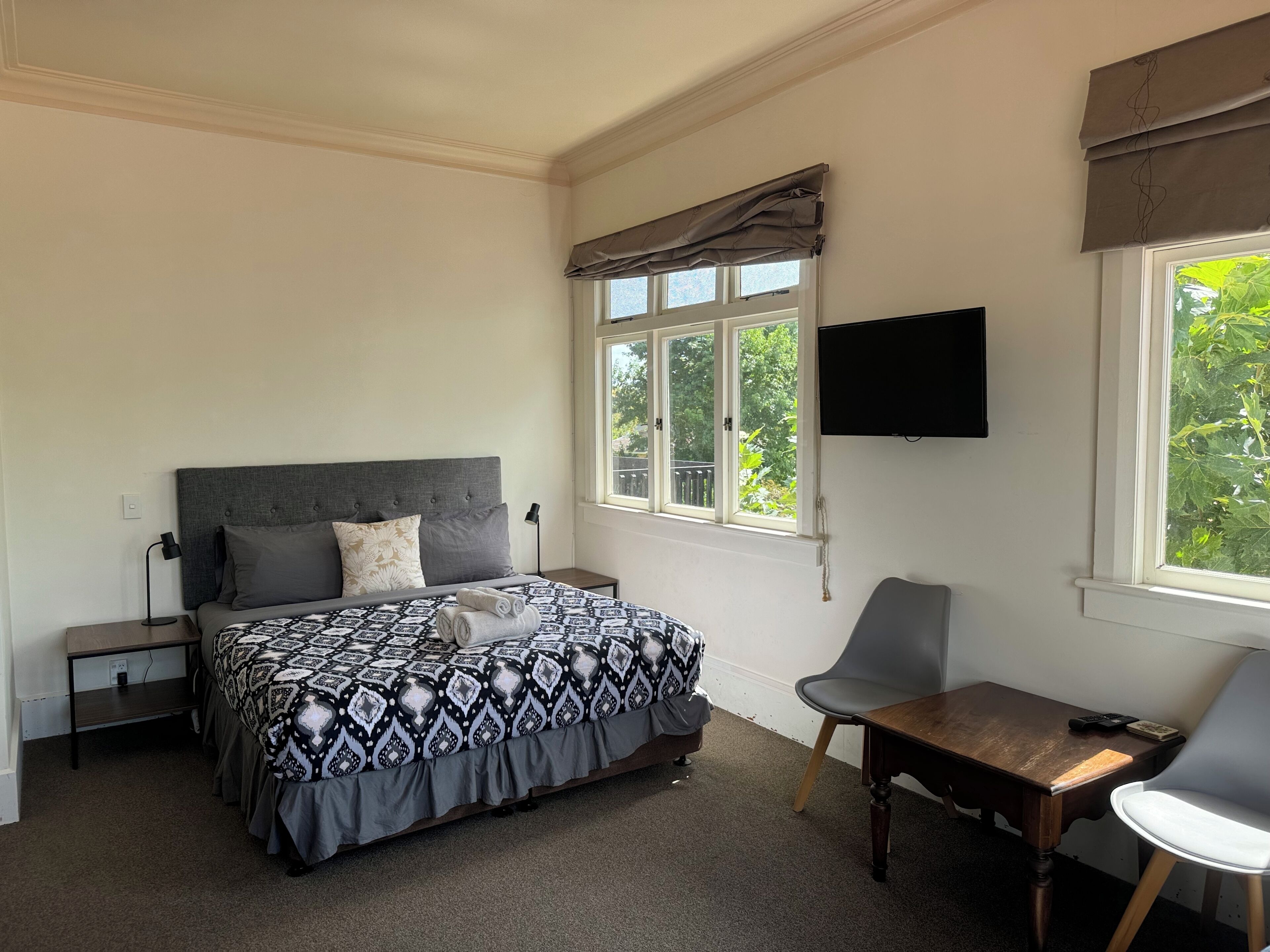 Un dormitorio con cama, escritorio, silla, televisor y ventana con vista a zonas verdes.