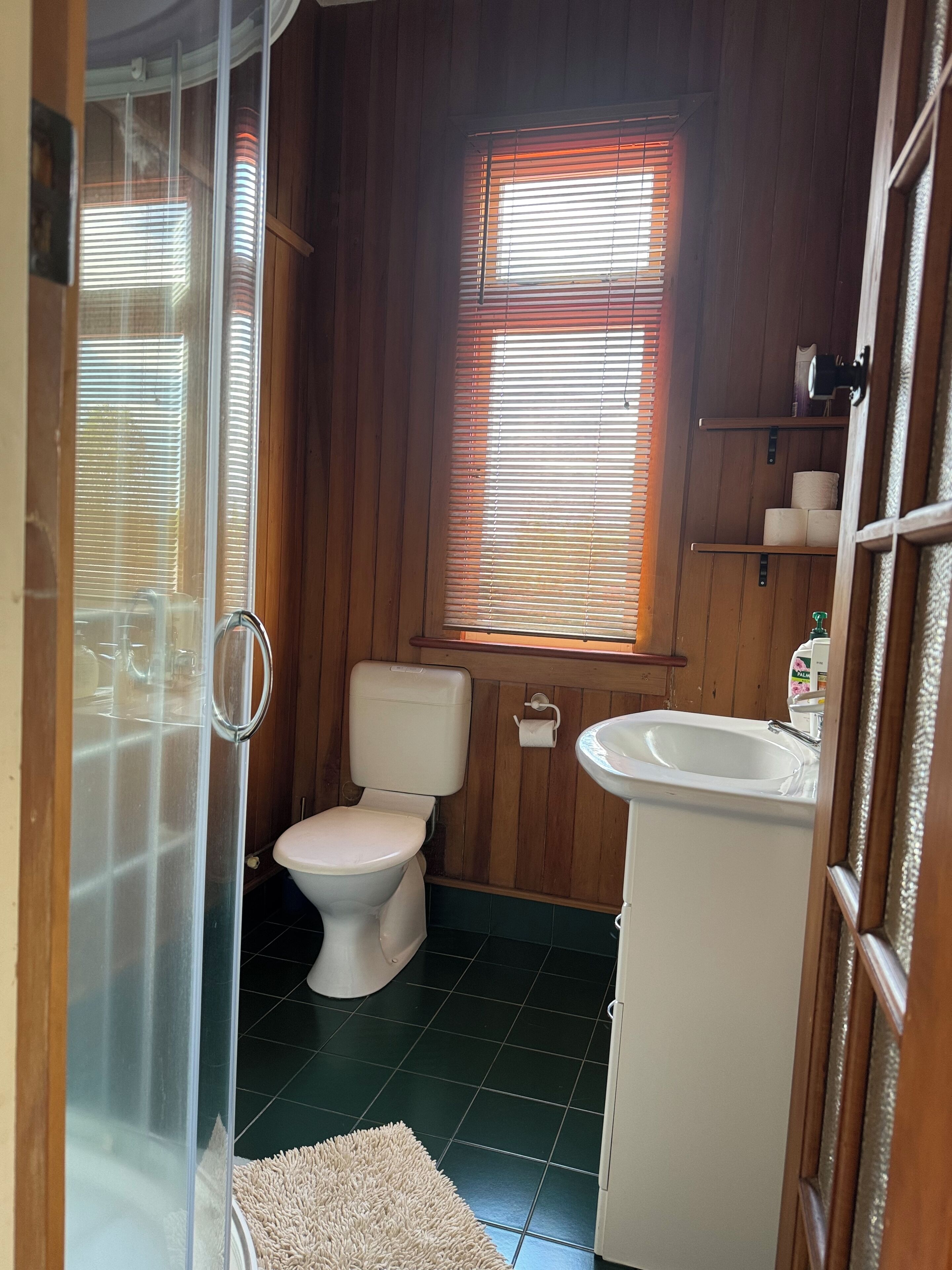 A small bathroom with a toilet, sink, and window with blinds.