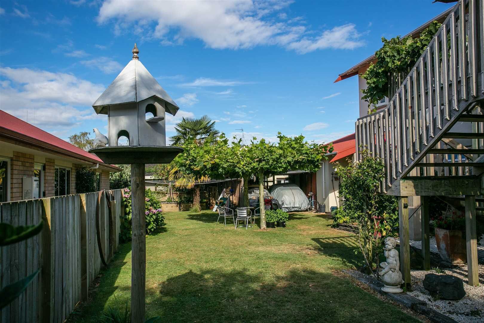 Un patio trasero con un comedero para pájaros, una zona de barbacoa cubierta y una valla de madera.