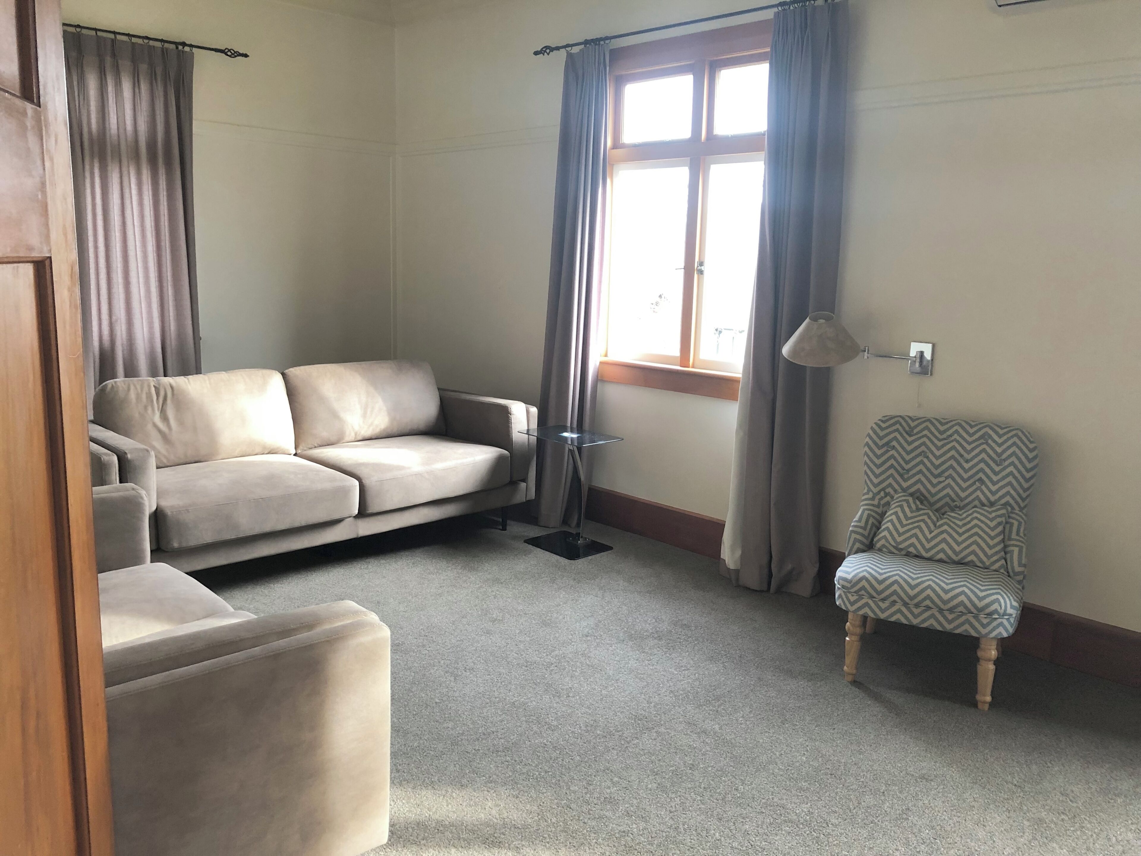 Une pièce comprenant un canapé, un fauteuil, une fenêtre avec des rideaux et une lampe.