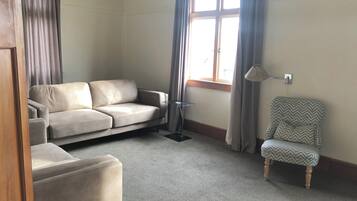 Una habitación con sofá, una silla, una ventana con cortinas y una lámpara.