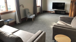 A living room with a sofa, armchair, and a television on a stand. - Penmarric House - Self Check-in (Cambridge)