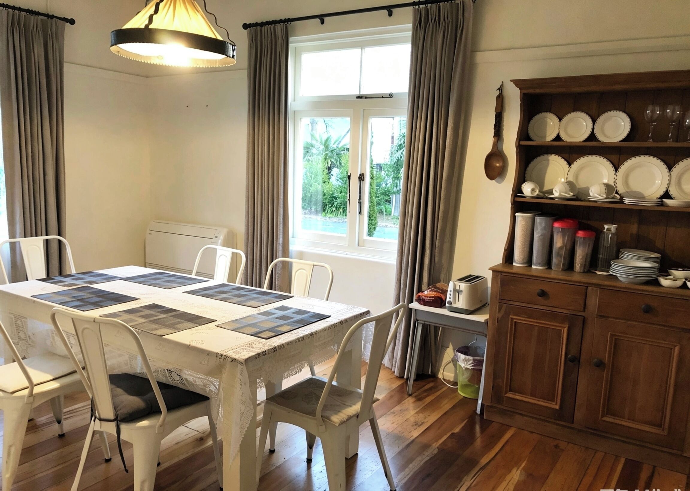 A dining area with a table set for four, a window with curtains, and a wooden cabinet with dishes.