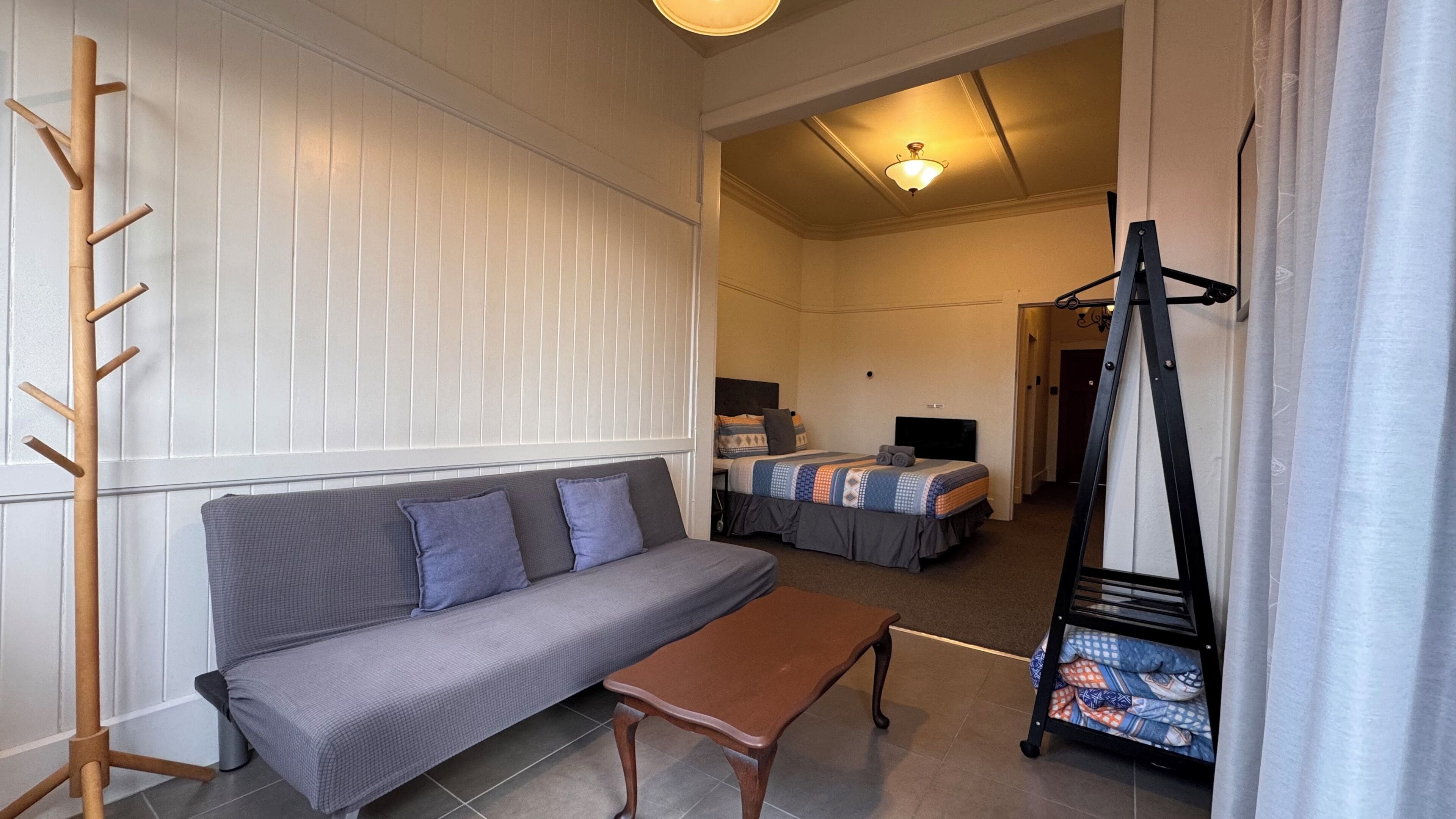 A room with a sofa, a small table, a bed with a TV, and a coat rack.