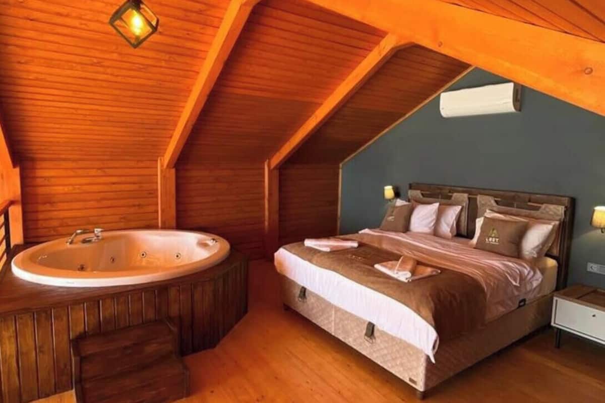 Une chambre avec un plafond en bois, un grand lit, une baignoire et un luminaire suspendu.