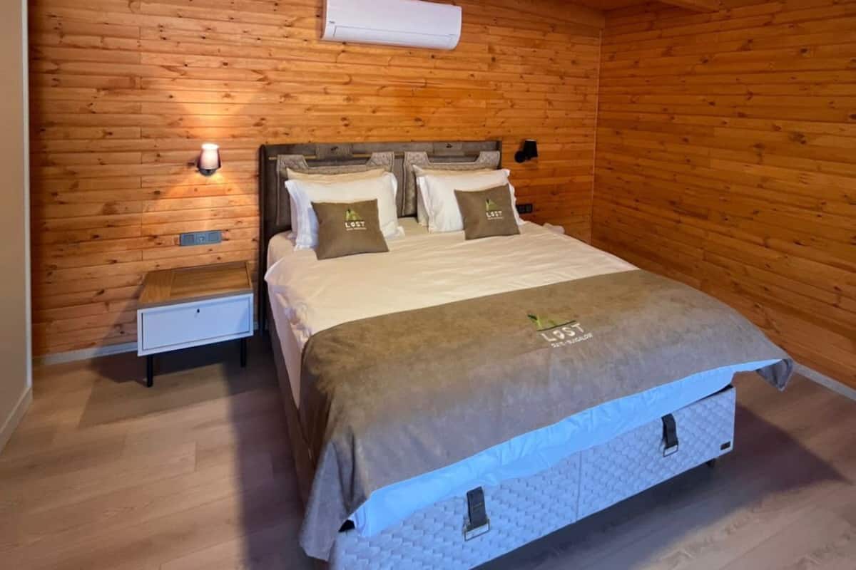 Une chambre aux murs lambrissés, avec un lit, des tables de chevet et un climatiseur fixé au mur.