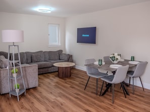 A modern living room with a grey sofa, a coffee table, and a dining area with chairs and a table. - Cozy Bungalow Retreat in Edinburgh (Edinburgh)