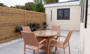 An outdoor patio with a round glass table surrounded by wicker chairs, a wooden fence, and a building with a window. - Cozy Bungalow Retreat in Edinburgh (Edinburgh)