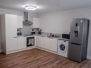 A modern kitchen with white cabinetry, a stainless steel refrigerator, a built-in oven, and a washing machine. - Cozy Bungalow Retreat in Edinburgh (Edinburgh)