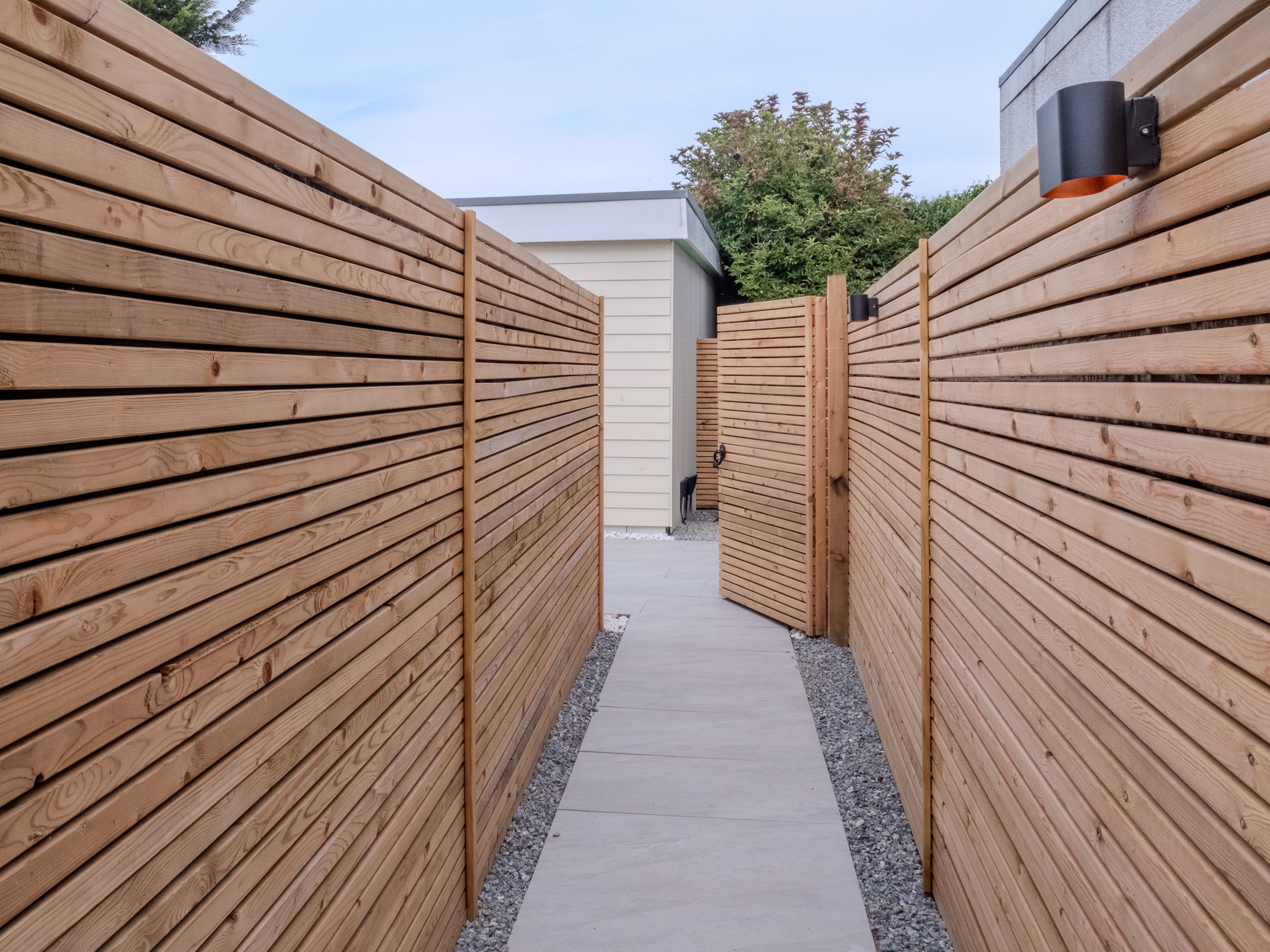 A narrow pathway flanked by wooden fences leading to a building.