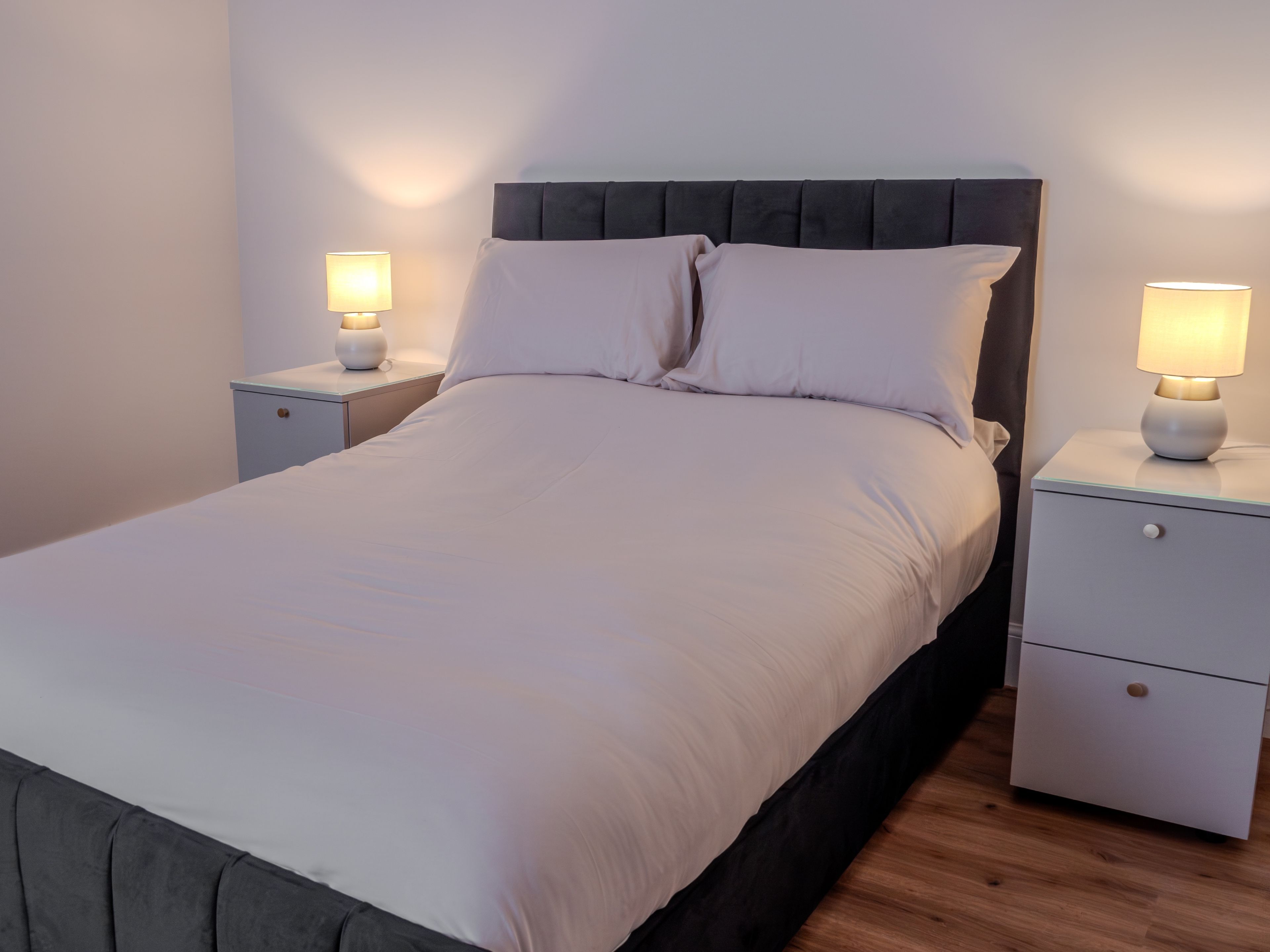 A neatly made bed with a headboard, two bedside tables with lamps, and a drawer unit.