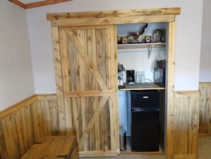 A kitchen with wooden paneling, a black refrigerator, and a shelf with various items. - Desert Serenity – Private 3BR/2BA Retreat Near Moab & National Parks (Moab)