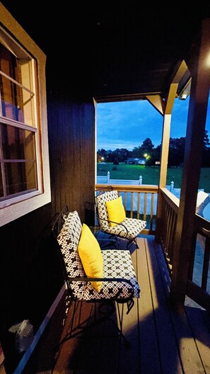 A porch with two chairs and a table, overlooking a grassy area with a fence.