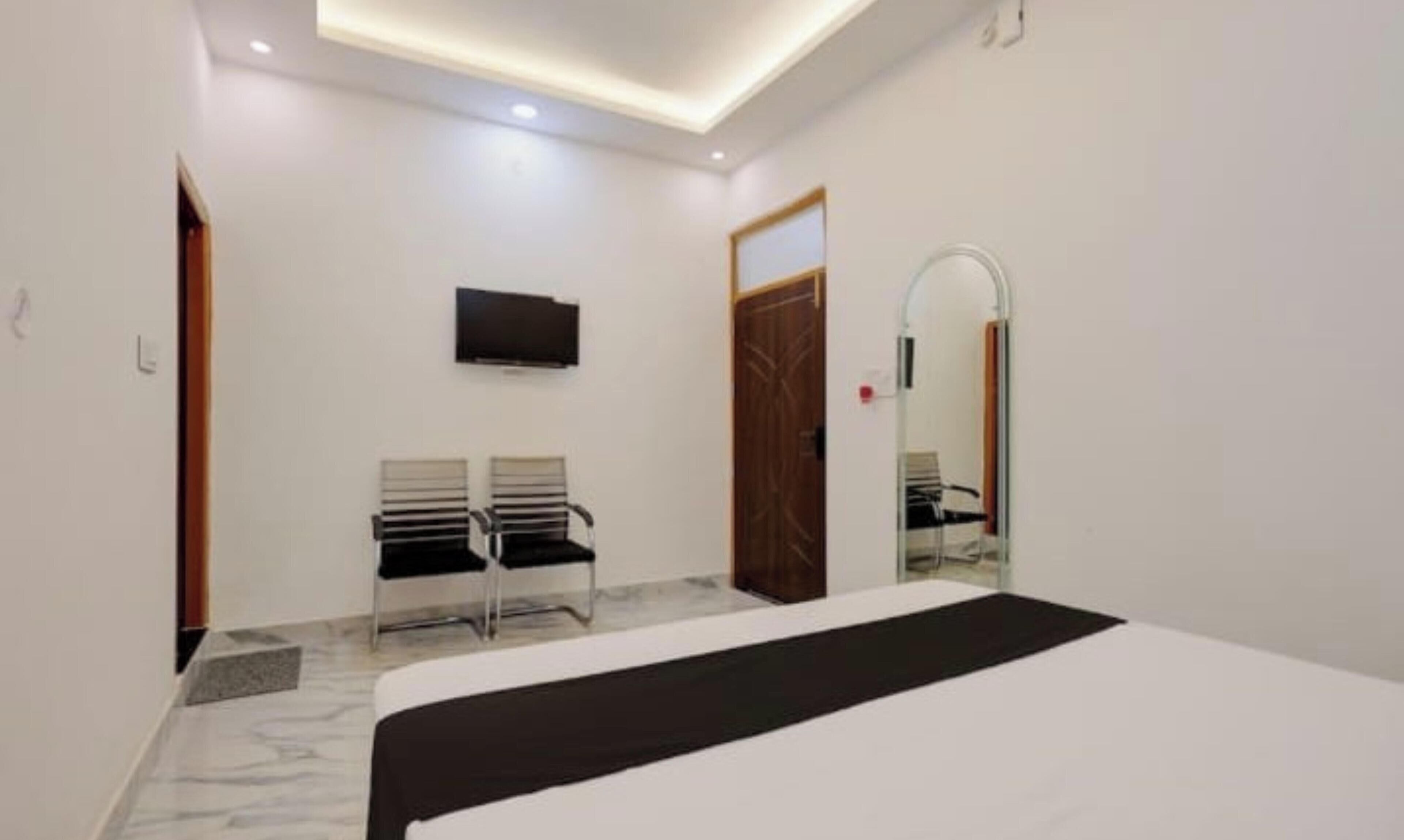 Un dormitorio con cama, televisor montado en la pared, una puerta y un espejo.