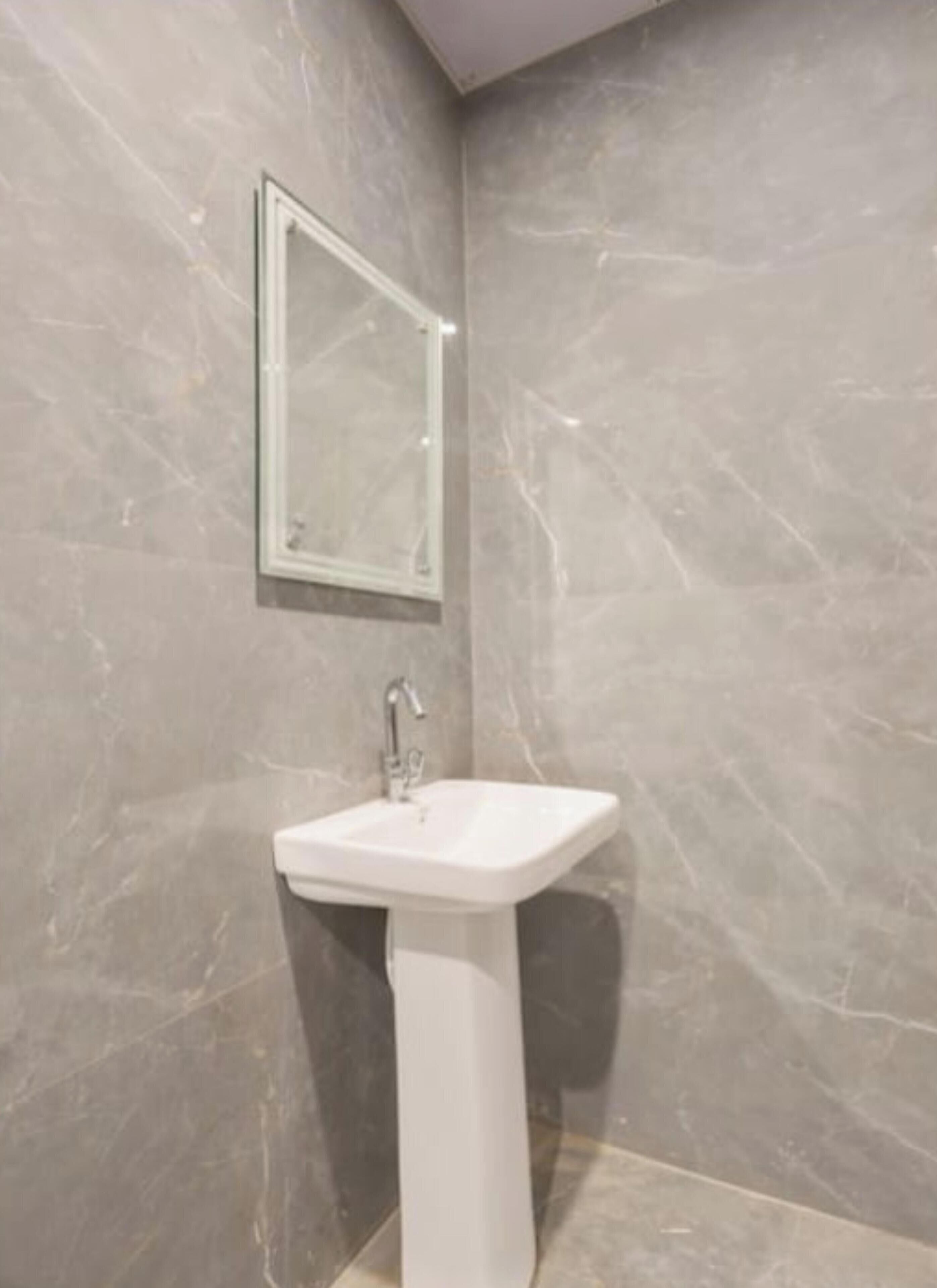 Un baño con lavamanos pedestal, un espejo y paredes de mármol.