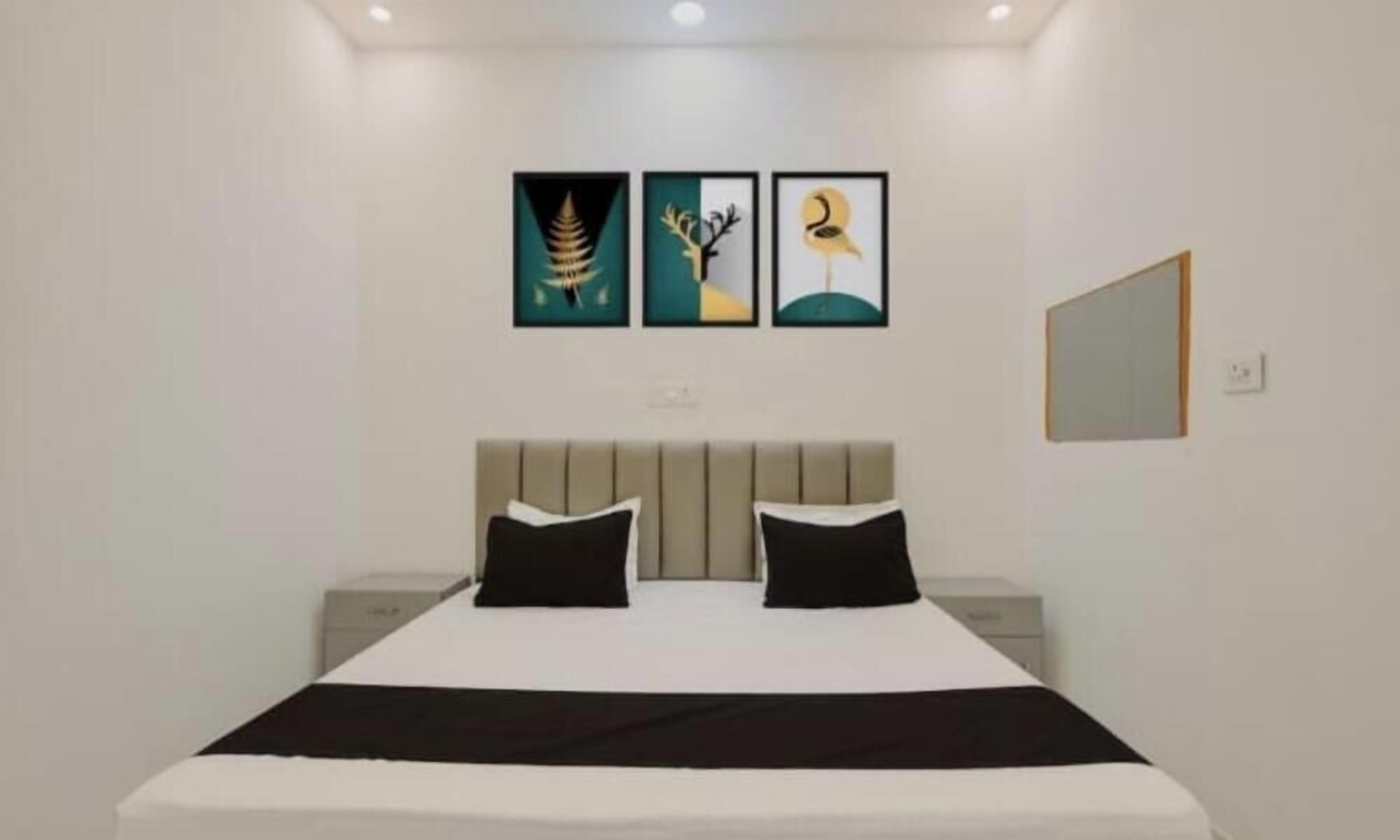 Habitación de hotel con cama, dos almohadas negras, cabecero, mesita de noche y tres cuadros en la pared.