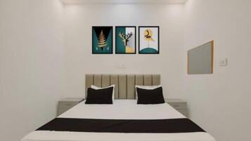Habitación de hotel con cama, dos almohadas negras, cabecero, mesita de noche y tres cuadros en la pared.