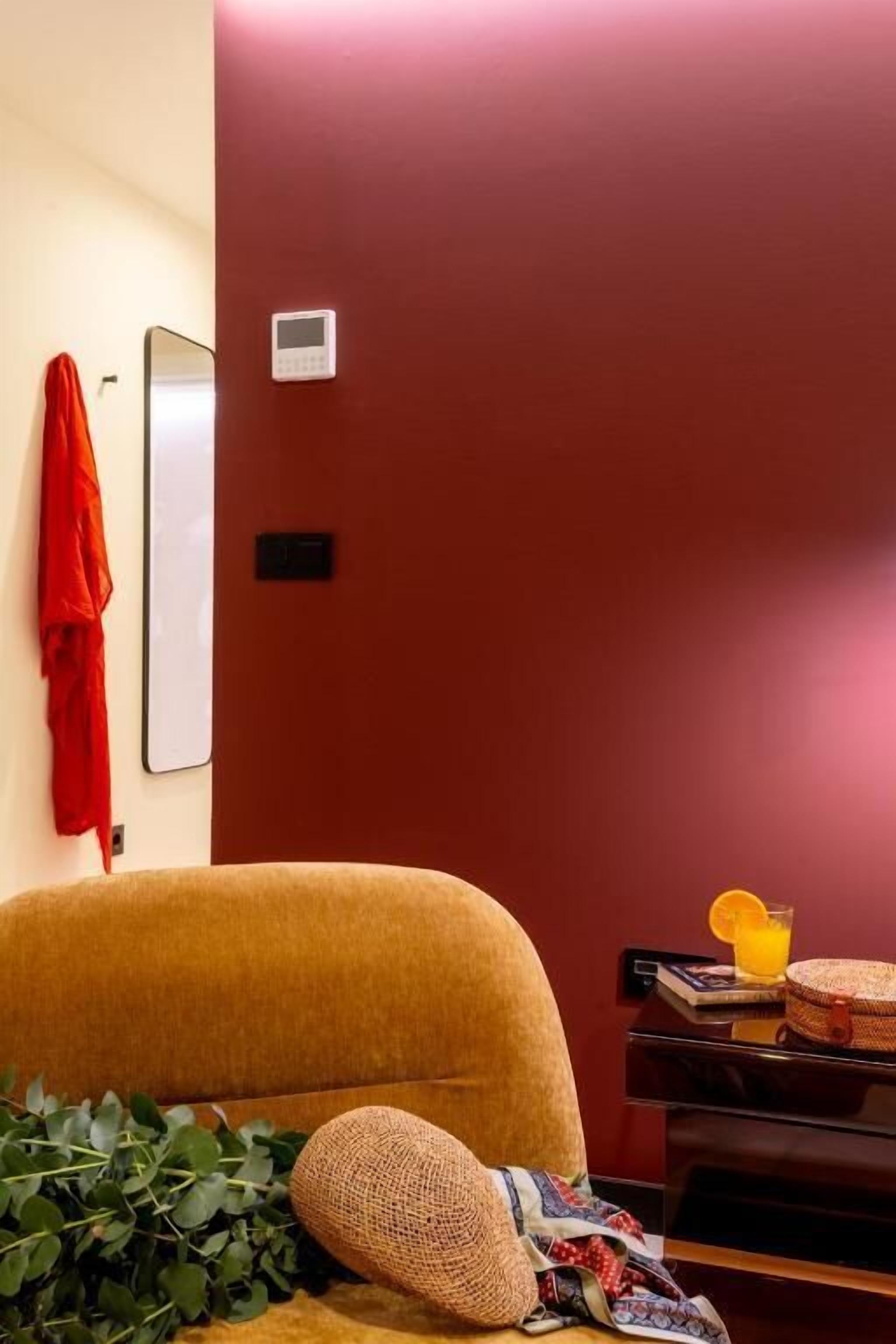 Una stanza con un divano marrone, una parete rossa, un tavolino con un cesto e un asciugamano rosso appeso al muro.