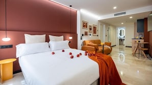 Una habitación de hotel con una cama grande, una sala de estar con mesa y una kitchenette.