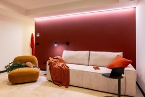 A modern living room with a sofa, a small armchair, a red wall, and a laptop on a side table. - VORS&Co Jerez (Jerez de la Frontera)