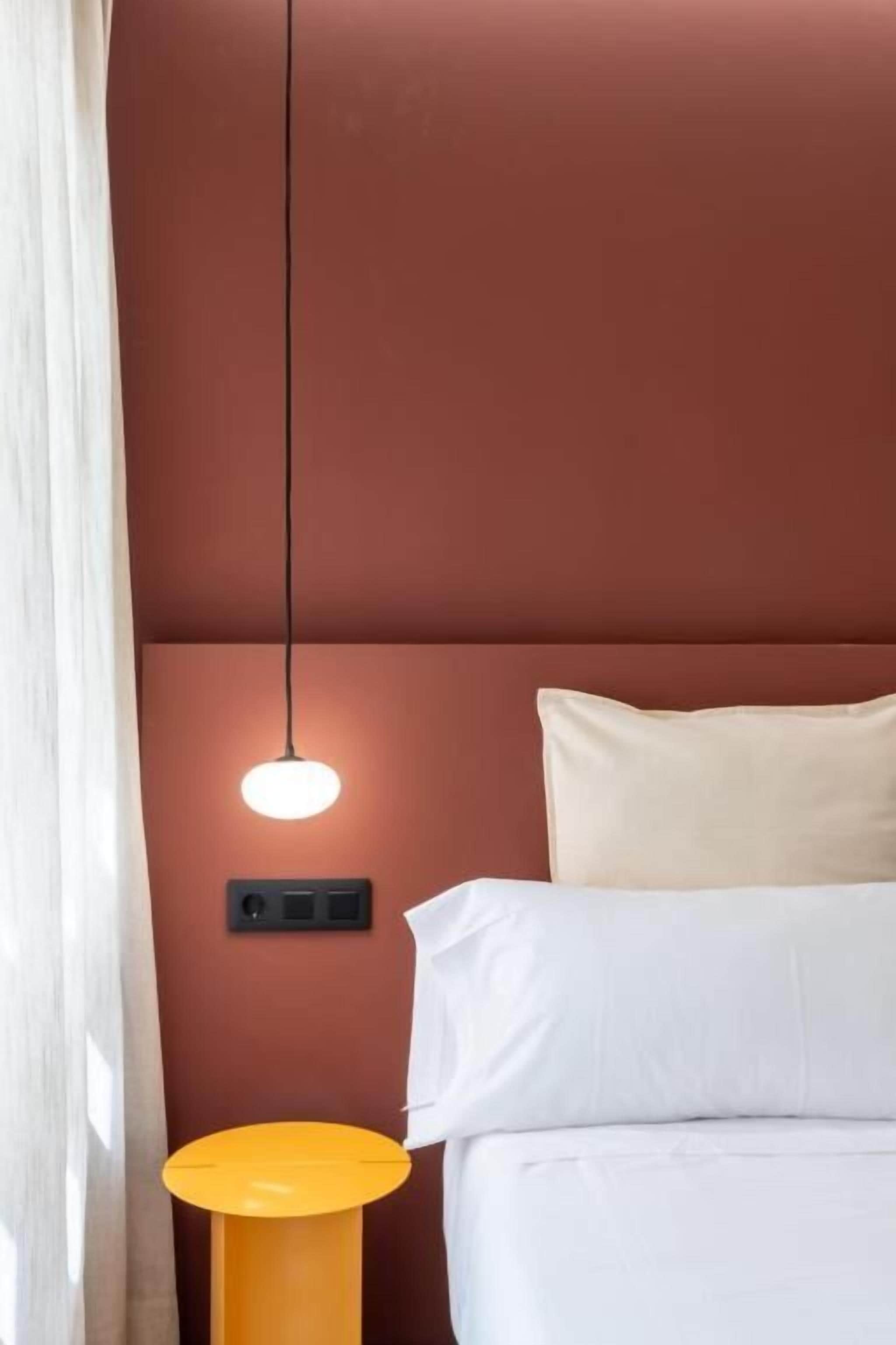 Una cama con ropa de cama blanca, un cojín beige y una mesita de noche amarilla.